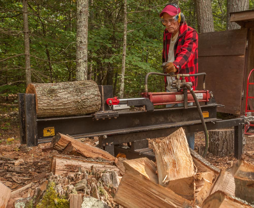 Older man using log splitter near a wood shed